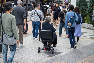 Tokyo, Japonya, 5 Kasım 2023: Tekerlekli sandalye kullanıcısı ile çeşitli kalabalık caddeleri geçiyor.