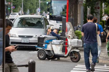 Tokyo, Japonya, 5 Kasım 2023: Yoğun şehir caddesinde motosiklet üzerinde dinlenen kurye.