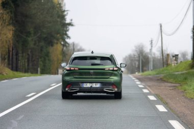 Fransa, 30 Mart 2024: Baharın başlarında yeşilliklerle çevrili manzaralı bir kır yolunda giden yeşil araba