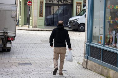 Fransa, 10 Mart 2024: Bir adam Perigueux 'nun sessiz sokaklarında tek başına yürüyor, plastik bir torba taşıyor, günlük hayatın basitliğini somutlaştırıyor..