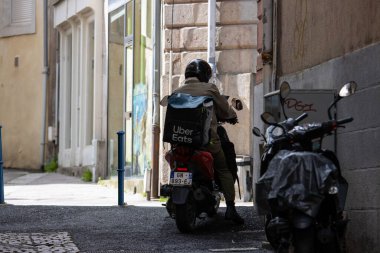 Fransa, 30 Mart 2024: Bir Uber, dar bir şehir caddesinde scooterlı teslimatçı.