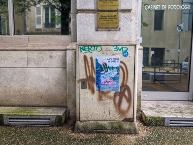 France, May 5, 2024: Graffiti-tagged urban bulletin board with flyers on a city street.