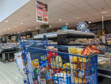 France, 8 May 2024: Grocery cart filled with various food items in supermarket aisle clipart