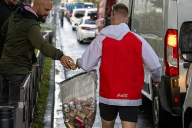 Fransa, 22 Mayıs 2024: Coca-Cola ceketli adam yağmurlu sokakta kutu topluyor