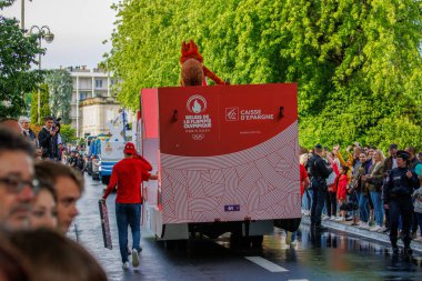 Fransa, 22 Mayıs 2024: Arka planda maskot ve kalabalık bulunan Olimpiyat bayrak aracı