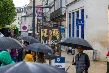 France, 22 May 2024: People with umbrellas walking in the rain in front of LCL bank and billboard clipart