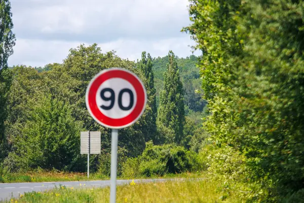 stock image France, 1 July 2024: Speed limit sign 90 km/h on rural road surrounded by trees