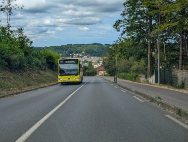 Fransa, 13 Ağustos 2024: Yeşil alanlarla çevrili kırsal bir yolda giden sarı otobüs