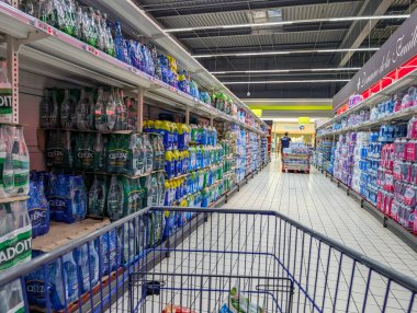 Fransa, 27 Ağustos 2024: Süpermarket koridorunda içi şişe su ve içeceklerle dolu bir alışveriş arabası