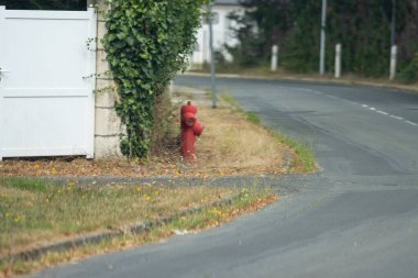 France, 15 August 2024 : Red fire hydrant by white fence on winding neighborhood road clipart