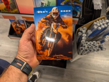 France, 19 August 2024: Hand holding a motorcycle-themed 2024-2025 calendar in a store clipart