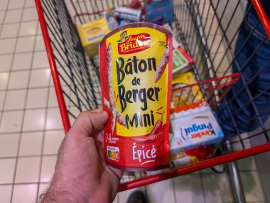 Fransa, 12 Ağustos 2024: Bir süpermarketteki alışveriş arabasında bir paket mini baharatlı sosis tutuyor