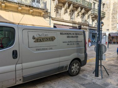 Fransa, 13 Ağustos 2024: Tarihi bir şehir meydanında mobilya yenileme reklamı olan beyaz minibüs