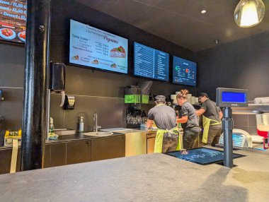 Fransa, 11 Eylül 2024: Üç restoran personeli dijital menü ekranları altında yemek hazırlıyor.