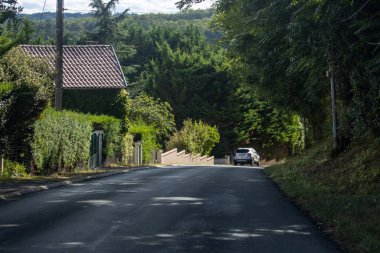 France, 08 September 2024 : Car drives down tranquil tree-lined street in rural neighborhood. clipart