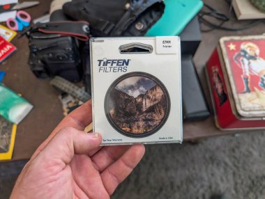 France, 13 August 2024 : Holding Tiffen Polarizer Filter Near Photography Equipment on Cluttered Desk clipart