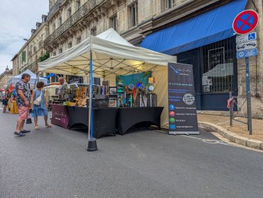 Fransa, 21 Ağustos 2024: Bir çadırın altında insanların baktığı el yapımı ürünlerin sergilendiği sokak pazarı