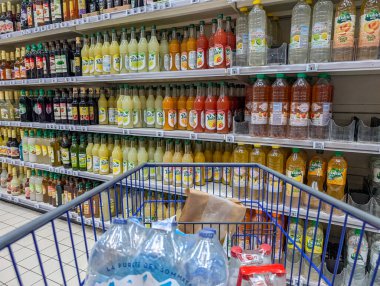 Fransa, 27 Ağustos 2024: Şişelenmiş meyve suyu ve içeceklerle dolu bir süpermarket koridorunda alışveriş arabası