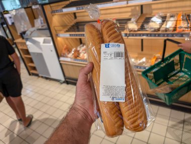 Fransa, 17 Ağustos 2024: Süpermarketin fırın bölümünde paket ekmek tutan kişi