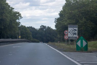 Fransa, 08 Eylül 2024: Yeşillik arkaplan ortasında yol kenarı işaretleri ve hız sınırı uyarısı.