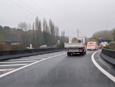 Fransa, 19 Kasım 2024: Bulutlu gökyüzü ve yol kenarındaki ağaçlarla ıslak karayolu trafiği