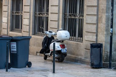 France, Bordeaux, 05 October 2024 : White Vespa parked near garbage bins on urban sidewalk. clipart