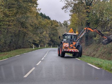 Fransa, 19 Kasım 2024: Yol kenarı bakım aracı orman yolu boyunca çimleri buduyor.