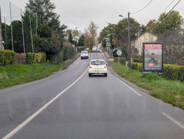 Fransa, 19 Kasım 2024: Yeşillikler arasında arabalı ve reklam tabelalı köy yolu