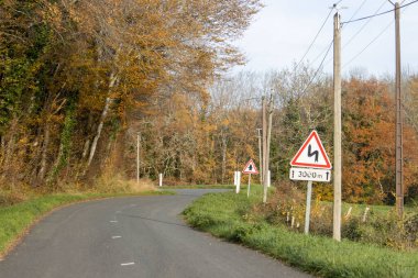 Fransa, 27 Kasım 2024: Sonbahar ormanı boyunca kıvrımlı yol ve ileride trafik işaretleri