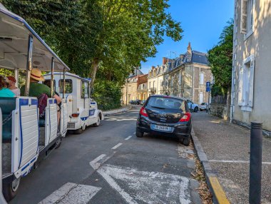 Fransa, 16 Ağustos 2024: Tarihi bir kasabada dar bir sokakta turist treni ve park halindeki araba