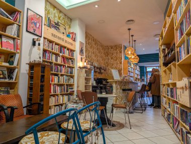 Fransa, 30 Kasım 2024: Ahşap rafları ve sıcak ışıklandırması olan samimi kitapçı kafe.