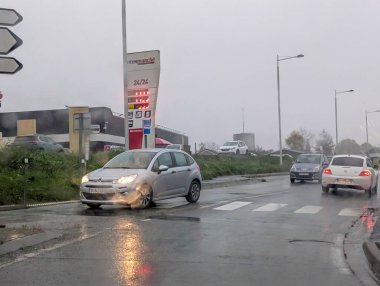 Fransa, 19 Kasım 2024: Yağmurda benzin istasyonu yakınlarındaki ıslak yolda giden arabalar