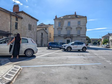 Fransa, 16 Ağustos 2024: Kadın tarihi binalarla küçük kasaba meydanında arabaya biniyor