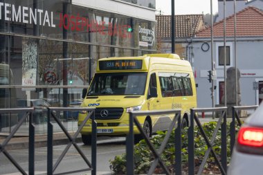 France, 07 December 2024 : Yellow bus travels past building with red lettered sign clipart