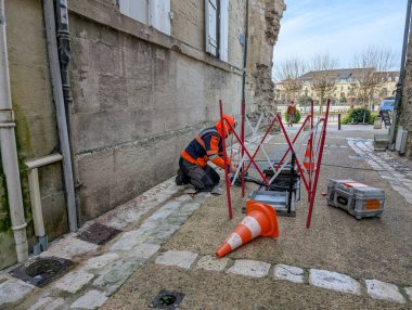 Fransa, 17 Aralık 2024: İşçi güvenlik konilerinin yanında sokak onarım kabloları üzerine diz çöktü