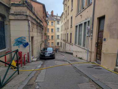 Fransa, Lyon 04 Şubat 2025: Park halindeki arabası, grafitisi ve sarı hortumu olan Dar Sokak.