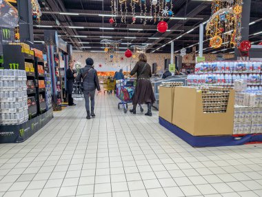 Fransa, 07 Aralık 2024: Süpermarket müşterileri kapalı mekanlarda tatil temalı koridorlarda yürüyorlar
