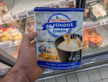 Fransa, 28 Mart 2025: Süpermarket peynir reyonunda paketlenmiş fondü tutan adam dondurulmuş