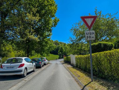 Fransa, 25 Nisan 2025: Park halindeki arabalarla, ağaçlarla ve yakındaki dur işaretleriyle güneşli banliyö caddesi