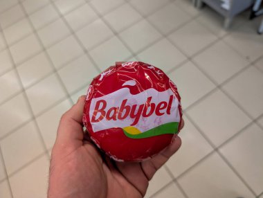 Fransa, 18 Nisan 2025: Büyük yuvarlak Babybel peynir paketini döşeme üzerinde tutan