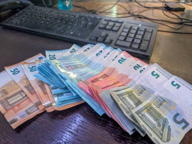 Fransa, 25 Mart 2025: Euro banknotları masaya yayıldı, bilgisayar klavyesinin yanına.