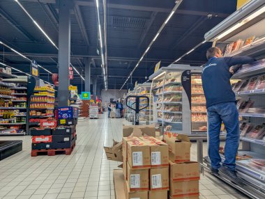 Fransa, 22 Nisan 2025: Çalışanlar paketlenmiş ürünleri raflara dizerken yoğun süpermarket koridoru