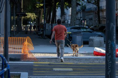 Fransa, 13 Mayıs 2025: Bir adam köpeğini caddedeki inşaat bariyerini aşarak yürütür.