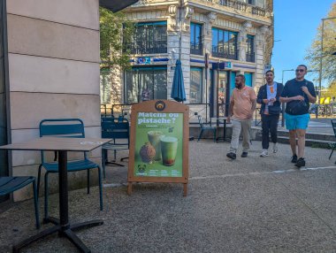 Fransa, 08 Nisan 2025: Menü tahtası ve yürüyen üç kişi ile açık hava kafe sahnesi