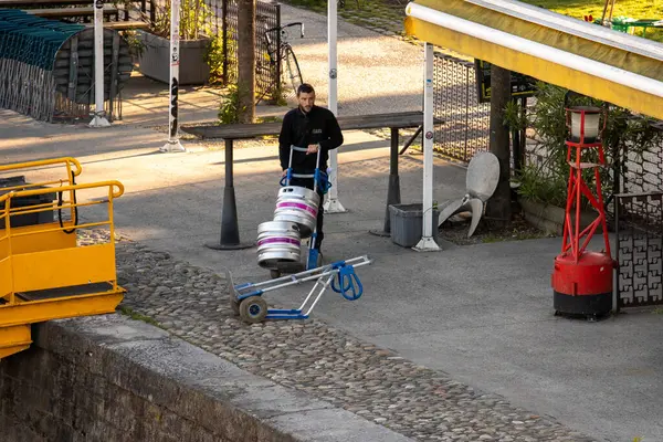 Fransa, 13 Mayıs 2025: Nehir kenarındaki kafe yakınlarında bira fıçıları taşıyan adam