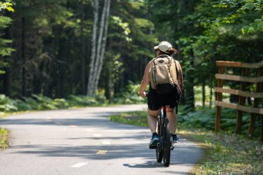 Quebec, Kanada, 15 Temmuz 2025: Huzurlu bir yaz sabahı orman yolunda bisiklet süren bisikletçi
