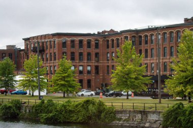 Quebec, Kanada, 08 Temmuz 2025: Bulutlu gökyüzü, tarihi tuğla bina, yeşil ağaçlar, arabalar ve nehir