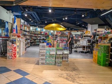 Quebec, Kanada, 07 Temmuz 2025: Sarı şemsiye rafları düzenleyen yoğun bakkal personelinin üzerinde duruyor.