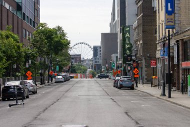 Quebec, Kanada, 06 Temmuz 2025: Park halindeki arabalar, ağaçlar, binalar ve uzak dönme dolap ile şehir caddesi
