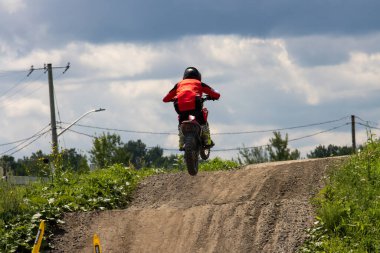 Quebec, Kanada, 20 Temmuz 2025: Kırmızı dişli motokros binicisi dışarıda toprak pistin üzerinden atladı